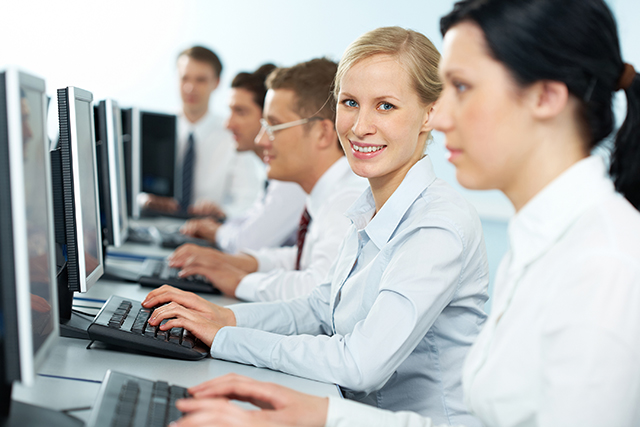 A businesswoman typing among her colleagues, looking at camera and smiling